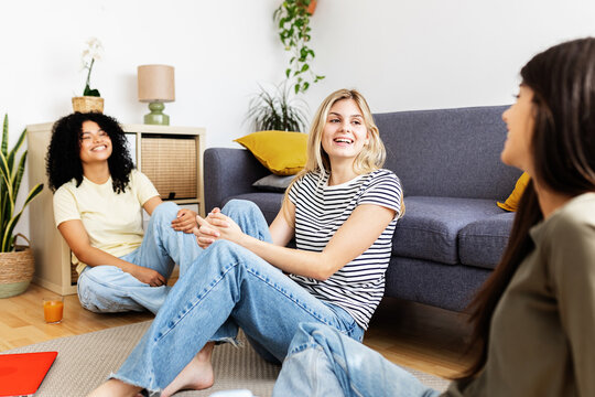 Three female students are sitting on a rug in their living room, enjoying a conversation and relaxing together. Female friendship and youth concept