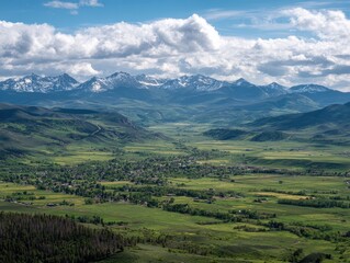 Obraz premium Panoramic vista of a verdant valley nestled between snow-capped mountains under a partly cloudy sky