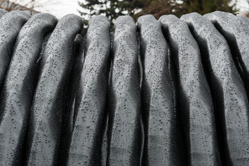 A close-up of a coil of black high-voltage electrical cable covered in raindrops