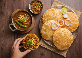 Spicy Indian chole curry served with crispy puri bread and garnished with fresh coriander, onion rings, and lime on wooden table, showcasing traditional vegetarian cuisine