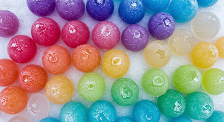 Colorful round ice balls arranged in rows on white surface showing gradient of vibrant colors from purple blue red orange yellow green to turquoise creating playful and refreshing visual effect