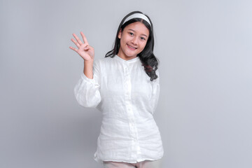 Cheerful young Asian woman in white outfit raising four fingers with a bright smile. Studio portrait with neutral background, perfect for advertising content.