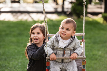 Older sister pushing baby brother on swing in backyard