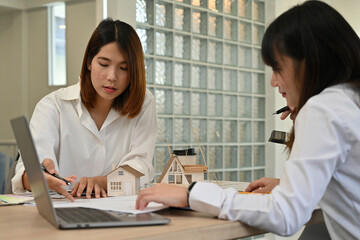 Two young female architects discussing construction ideas and project details at a work desk