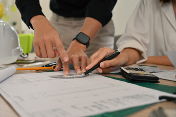 Close-up of engineers pointing at architectural plans, discussing precise measurements with a pen...