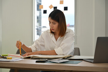 Young Asian woman architect using a compass to create precise drawings, working on architectural...