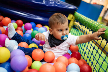 Baby boy playing with colorful balls in ball pit