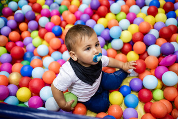Baby boy playing with colorful balls in ball pit