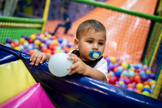 Toddler playing with pacifier and ball in colorful ball pit