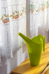 A green watering can sits on a wooden table next to a window