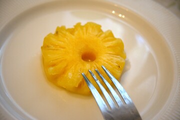 Pineapple ring on white plate with fork