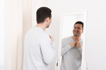 Handsome man looking at himself in mirror indoors