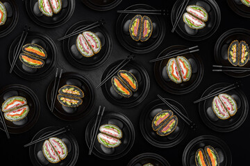 Top view of a lot of sushi burgers on a textured black background. A modern fusion of Japanese ingredients styled like a traditional burger. Unique and trendy food concept.