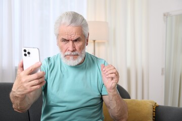 Senior man with vision problem using smartphone on sofa at home