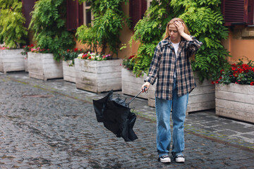 Frustrated woman with broken umbrella on city street. Space for text