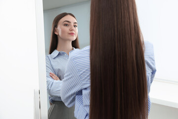 Beautiful woman looking at herself in mirror indoors