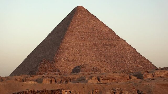 Camels walk past base of Khufu pyramid in golden Giza desert of Egypt