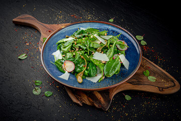 Fresh green spinach salad topped with parmesan cheese on a dark background. Healthy vegetarian dish with minimal presentation.