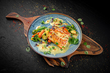 Baked salmon fillet served with a mix of vegetables on a dark background. Healthy gourmet dish.