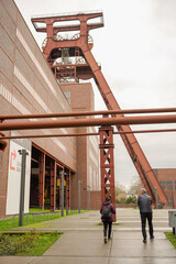 Two Elder people walking around Zollverein Coal Mine Industrial Complex with a coal mine tower in the background, Essen, Germany
