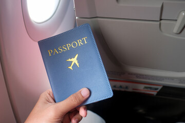 A person holding a blue passport wallet inside an airplane cabin with passengers and in-flight...