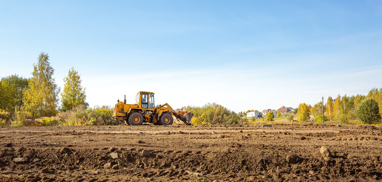 Yellow bulldozer at a construction site. Big wheel excavator leveling and clearing the land plot side view. Moving earthworks soil. Copy space. Building area. Special transport. High quality photo.