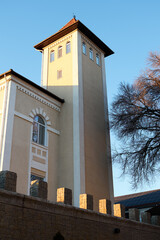 Sunlit tower of a beige building with arched windows and decorative brick wall © watcherfox