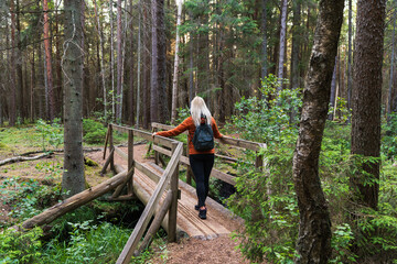 A female tourist with a backpack crosses a wooden bridge in a dense pine forest, enjoying the hike...