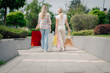 Two happy women walking away after shopping, carrying shopping bags