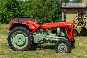 Obraz premium Classic red and green vintage tractor parked on grass, with visible engine details and large rear wheels. Surrounded by rural scenery and old agricultural machinery