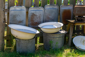 Fototapeta premium Collection of old enamel bowls and galvanized tubs arranged with rusty vintage washboards in a backyard. Rustic household scene with nostalgic charm.