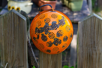 Rusty orange metal colander hanging on a wooden garden fence. Upcycled rustic decoration with...