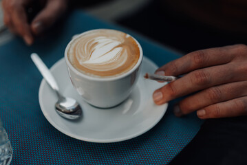 Customer holding cannabis cigarette enjoying cappuccino at outdoor cafe