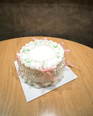 close up of vintage cake with pink bows of delicate cream color on a wooden table in a room.