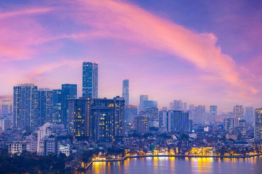 Hanoi skyline at sunset with pink clouds and illuminated buildings reflecting on water