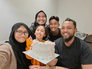 An Asian Muslim family celebrating a birthday together in their home.