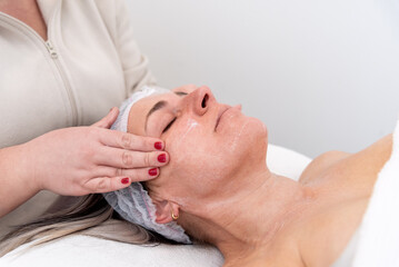Beautician applying cream on woman's face for facial treatment