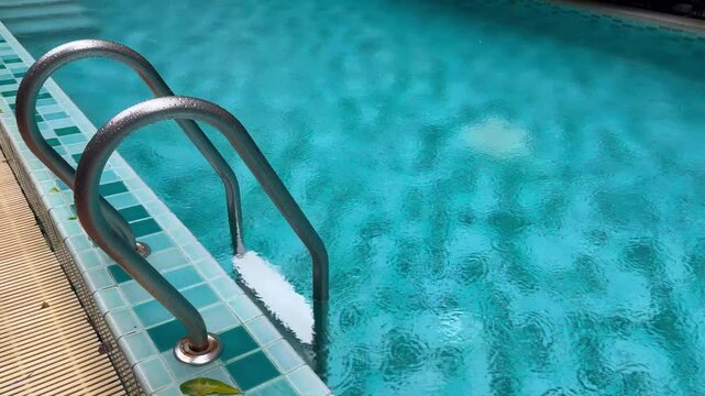 Light rain falling on the blue swimming pool, shot from the side of the pool.