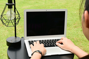 A woman is typing on a laptop in a park. The laptop screen is black, and the woman is focused on her work