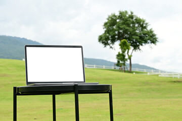 A laptop is open on a table in a grassy field. The grass is green and the sky is cloudy. The scene is peaceful and serene, with the laptop