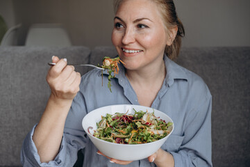 Smiling woman eats a salad with arugula and vegetables, healthy eating at home