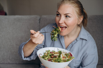 Smiling woman eats a salad with arugula and vegetables, healthy eating at home