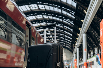 Black suitcase with wheels positioned on platform, train approaching in background, showcasing...