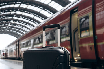 Black suitcase with wheels positioned on platform, train approaching in background, showcasing...