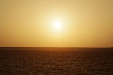 Sun melting into mirage above dusty horizon, extreme telephoto view, ethereal tone