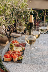 Outdoor dining or aperitif white wine glasses on a stone table with gourmet charcuterie board assorted meats, olives, and cheese