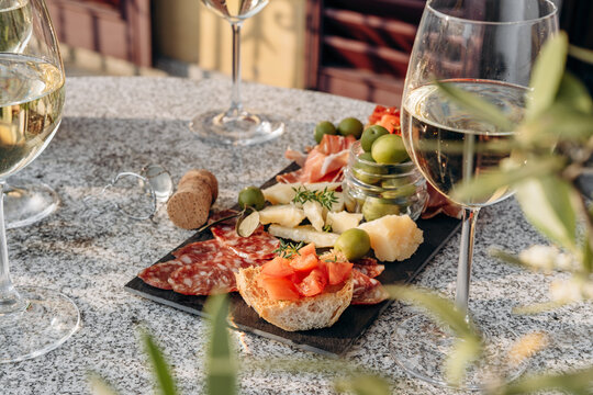 Food antipasto prosciutto ham, salami, olives and grissini bread sticks. cheese on a board parmesan, pecorino, gorgonzola. Charcuterie board. Two glasses of white wine or prosecco - Powered by Adobe