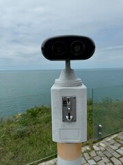 Public binocular viewer overlooking the sea on a cloudy day, mounted on a platform with coin slot....