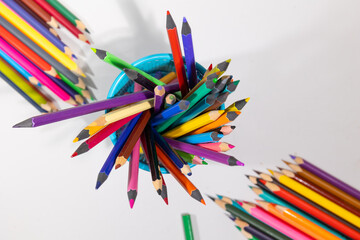 Pencils of various colors are organized in a blue holder, creating a vibrant display perfect for back to school. Surrounding the holder are additional pencils, adding to the school atmosphere.