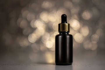 Fototapeta premium Sleek black serum bottle with gold dropper cap stands elegantly against blurred, shimmering background. soft bokeh effect enhances luxurious feel of product, making it ideal for skincare